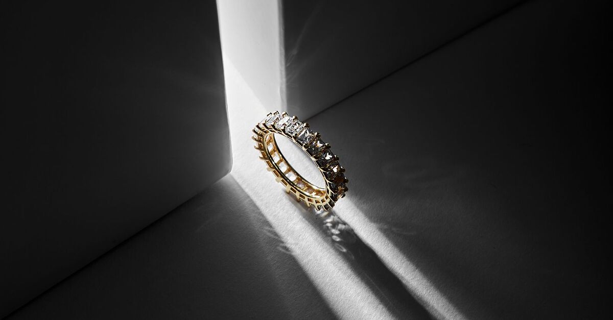 A gold and diamond ring standing in a single shaft of light against a dark background