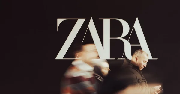 Blurred people walking past a black wall with a Zara logo