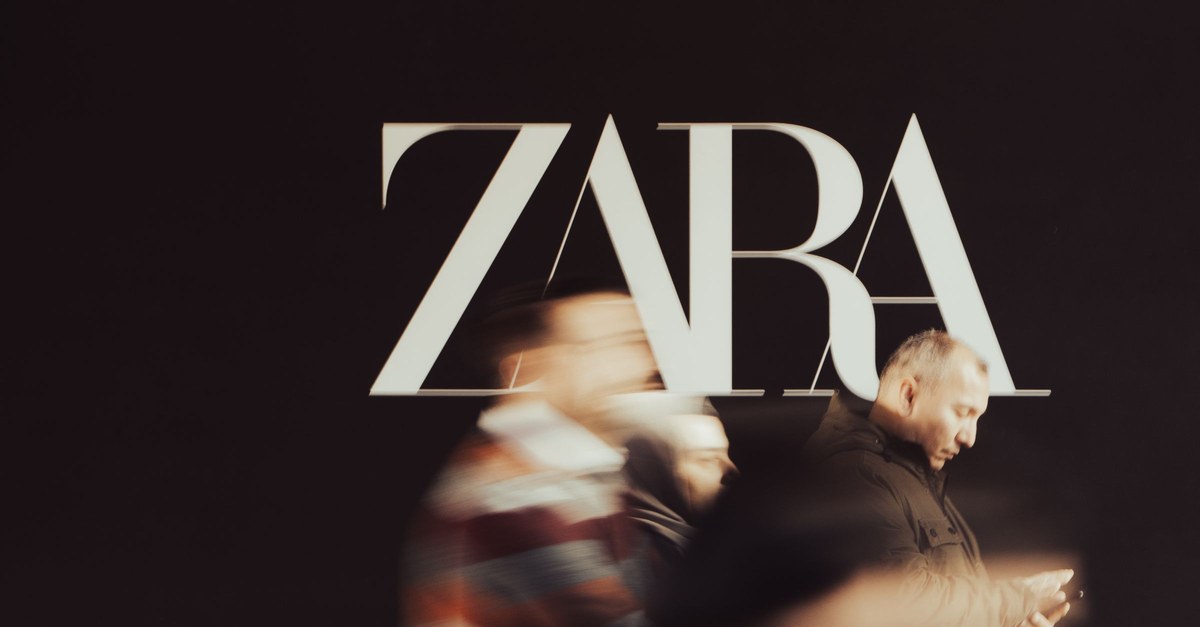 Blurred people walking past a black wall with a Zara logo